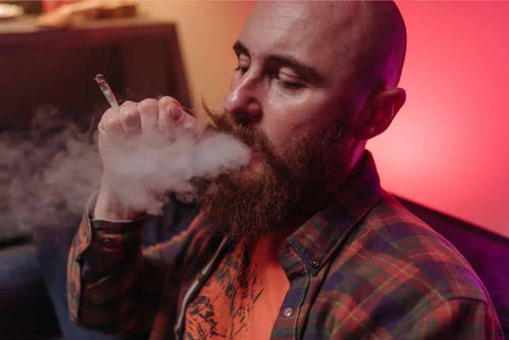 man with handlebar mustache exhaling smoke from joint