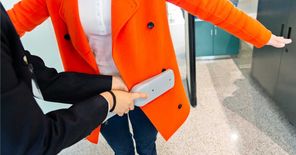 using metal detector wand on person with orange jacket