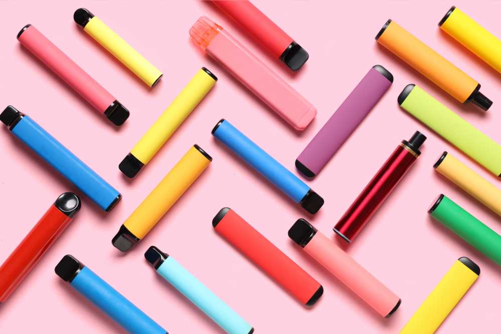 various colorful disposable vapes against pink background